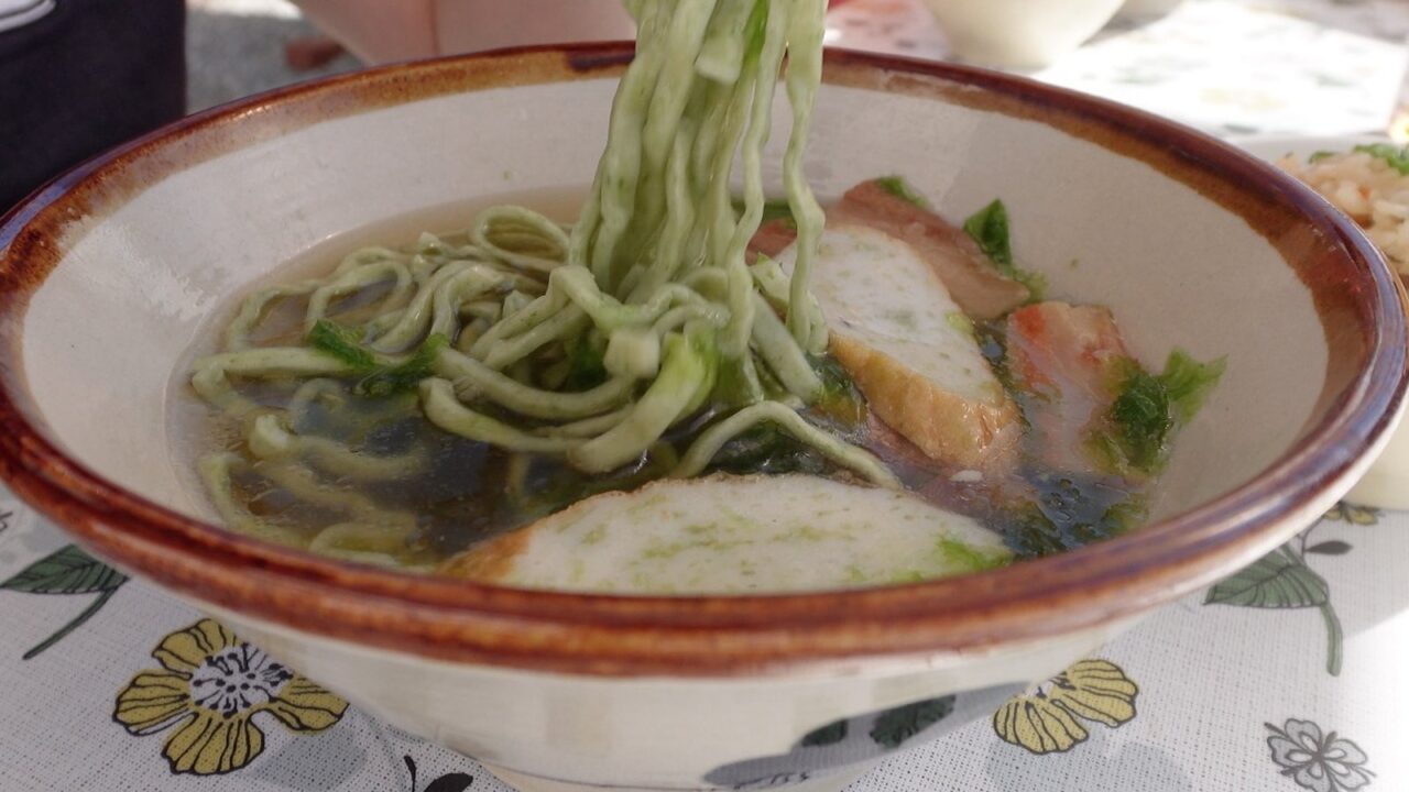 箸で持ち上げた緑色のアーサ麺となかむらそばのアーサそば